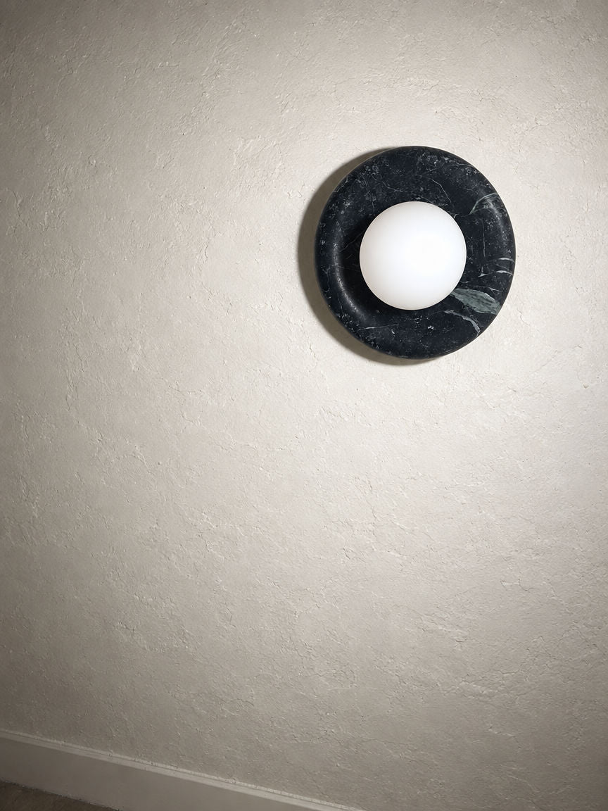 Orba Marble Wall Sconce in Nero, angled view on a plaster wall