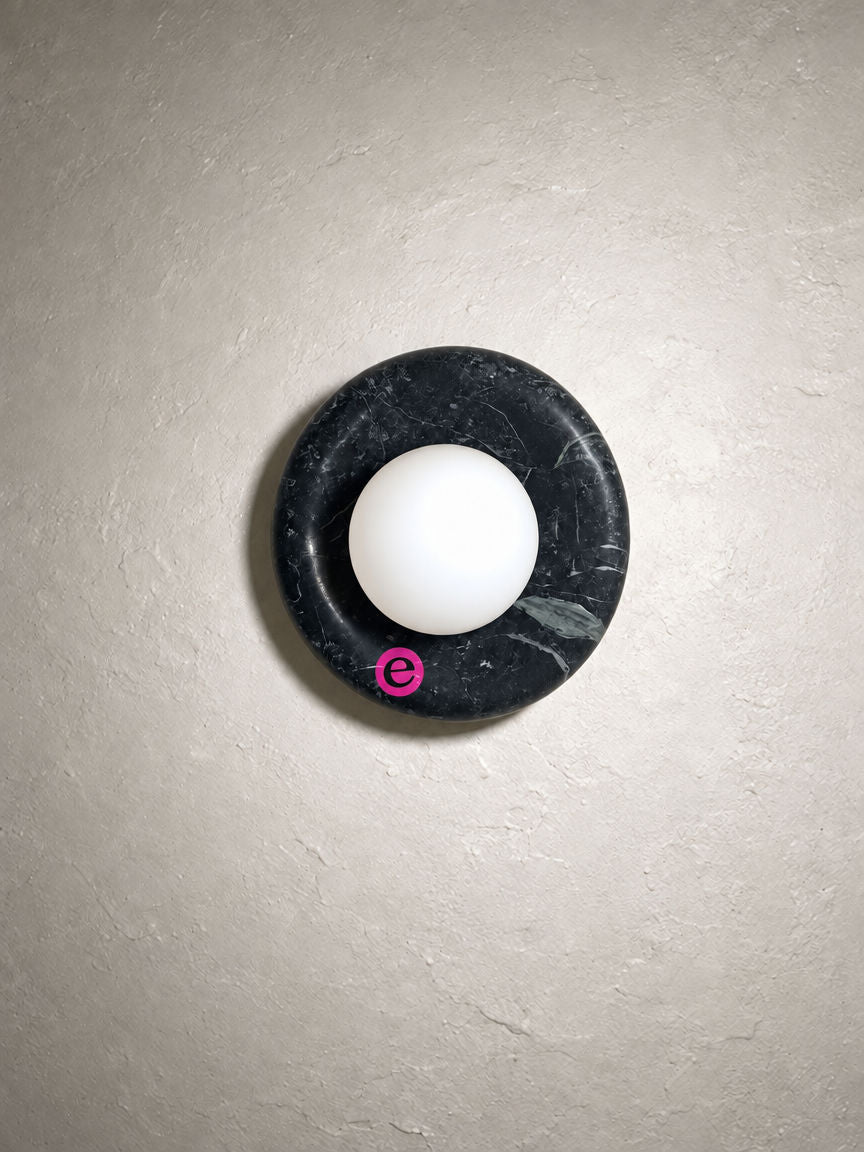 Orba Marble Wall Sconce in Nero on a plaster wall with an Estate sticker